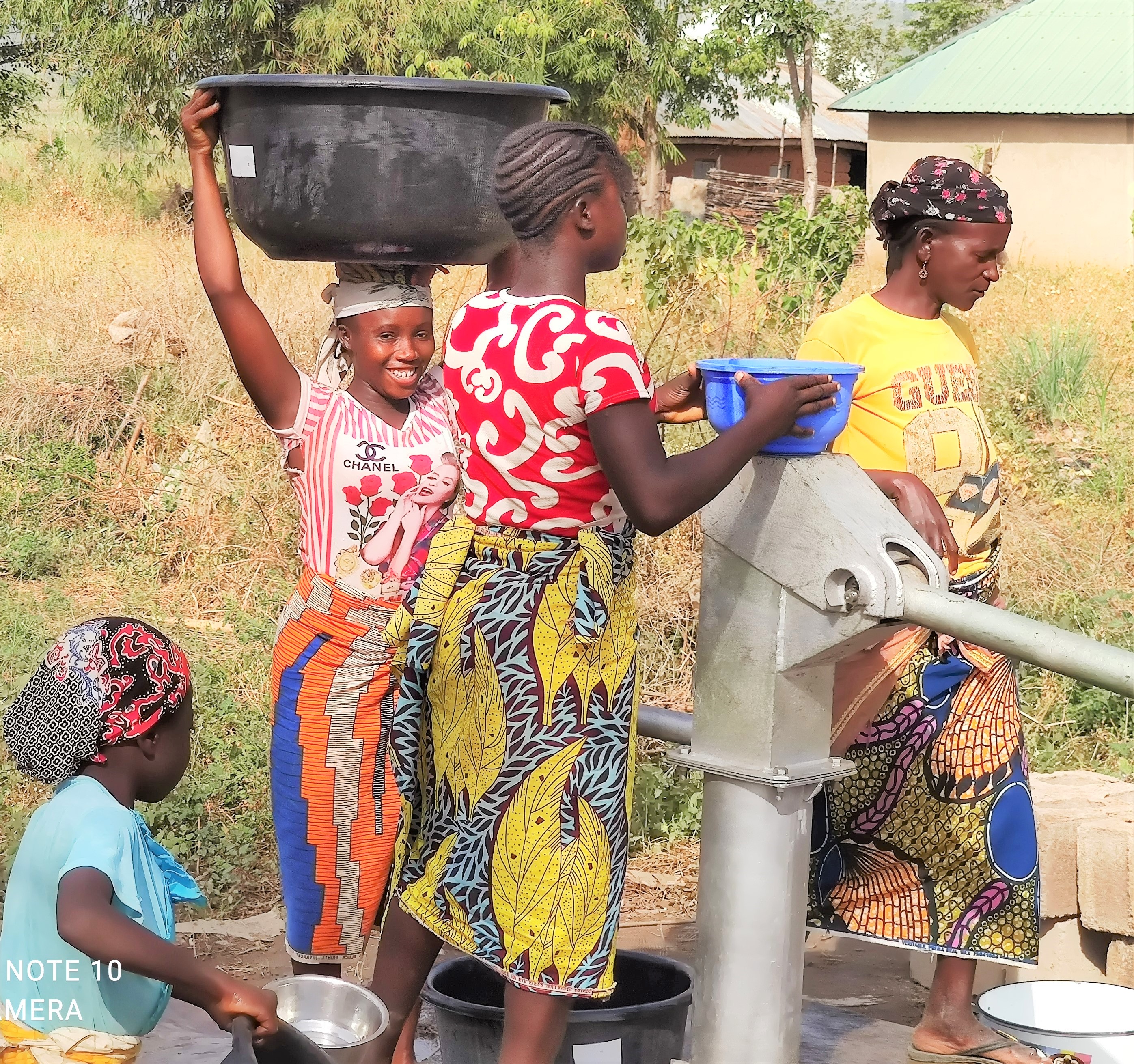 Smiling woman carries large bucket on her head next to a new well