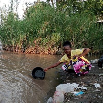 Village woman collecting water from a dirty river, community's previous water source 