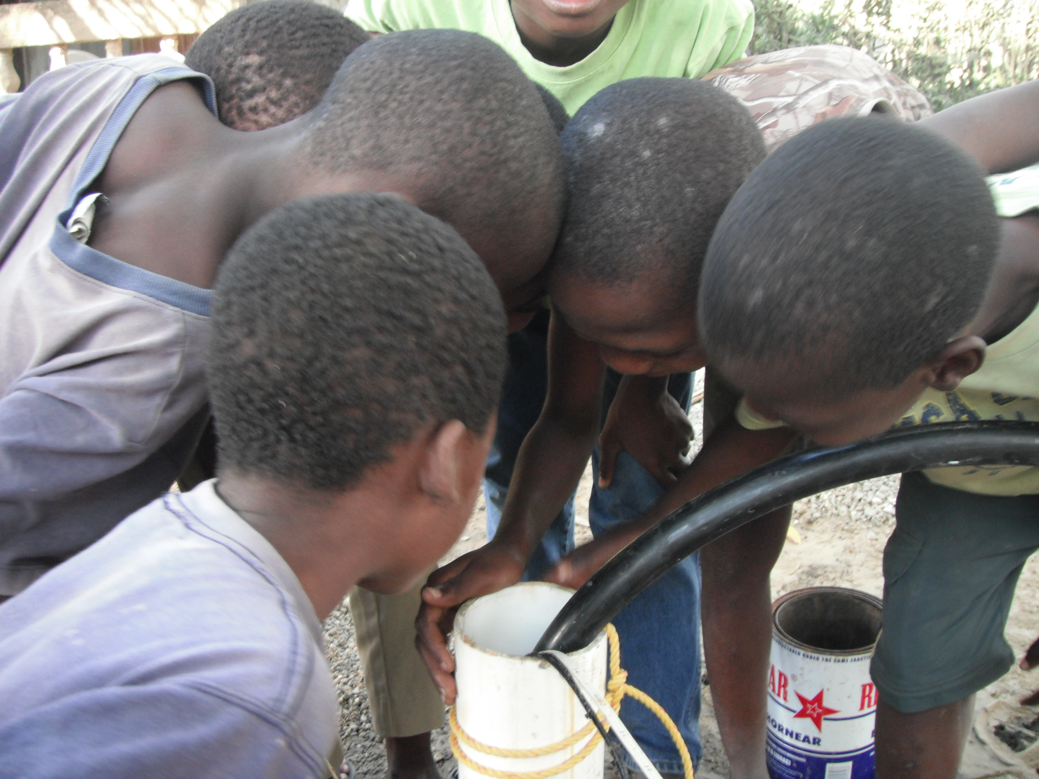Kids trying to look down the well to see how the hose was filling without a handpump!