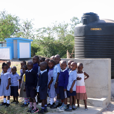 Students by new Catchment & Handwashing Station with Latrine in background