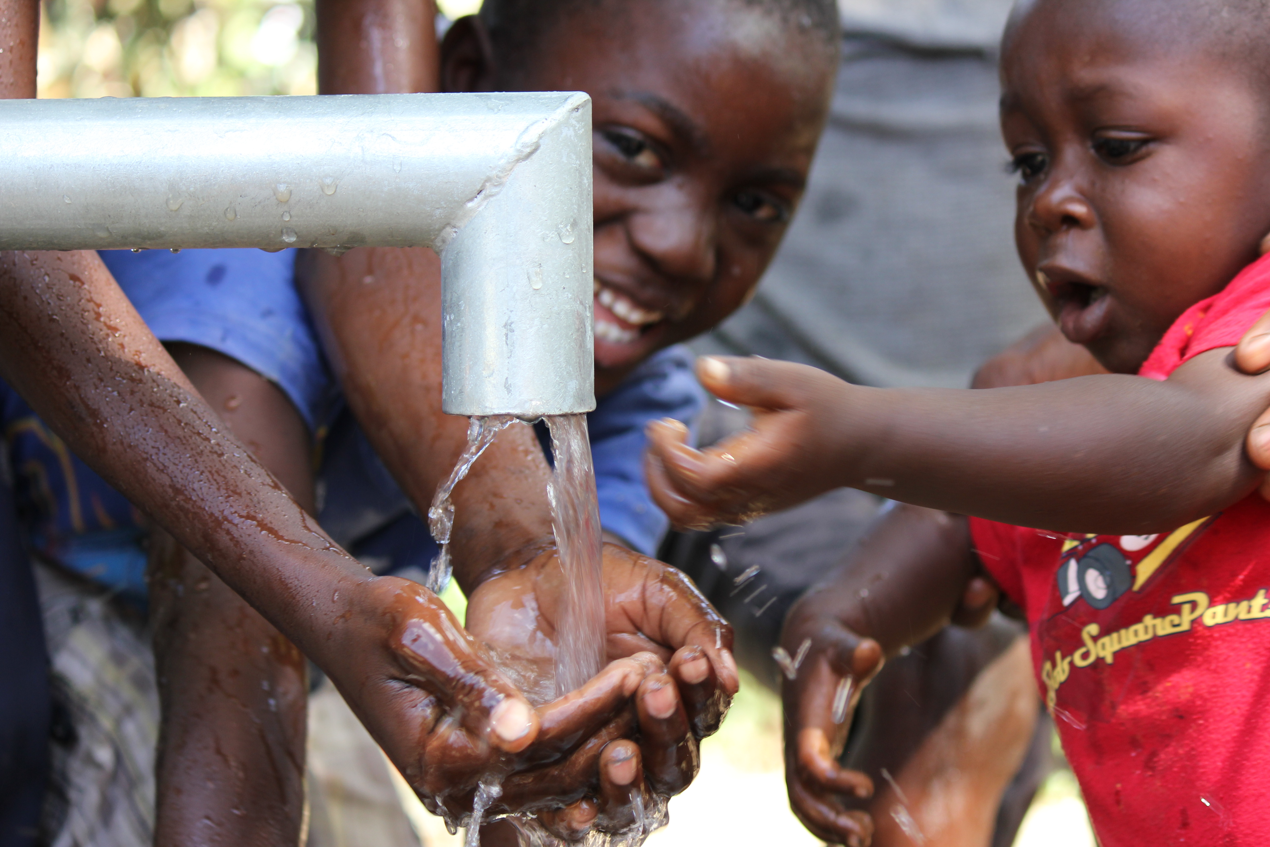 Children smiling as they run their hands under water from a hand pump